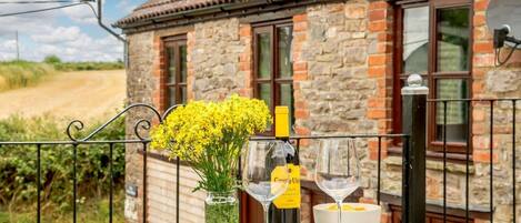 A balcony with a table set for two, featuring a bottle of wine, a glass, and a vase with yellow flowers.