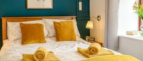 Een net opgemaakt bed met een beddegoed met bloemenprint, twee opgerolde handdoeken en een bedlamp.