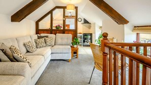 Ein Loft-Wohnzimmer mit einer Couch, einem kleinen Tisch und einem Korbstuhl. Eine Holztreppe führt auf eine erhöhte Ebene.