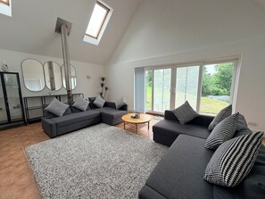Ein modernes Wohnzimmer mit einem Ecksofa, einem runden Couchtisch und einem großen Fenster mit Blick ins Freie.