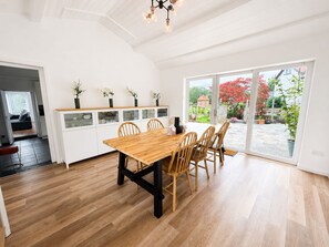 Ein geräumiger Essbereich mit einem Holztisch und Stühlen, einer weißen Kommode mit Glastüren und Blick auf einen Garten durch große Schiebetüren.