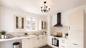 A modern kitchen with white cabinetry, a stainless steel trash bin, a gas stove, and a window providing natural light. - Luxury 5BDR Riverside Retreat near Uxbridge (Harefield)