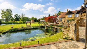 A serene riverside setting with stone pathways, a wooden bridge, and traditional houses. - Luxury 5BDR Riverside Retreat near Uxbridge (Harefield)