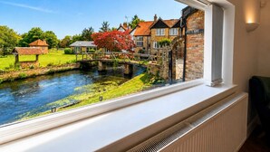 A view of a river with a bridge, stone buildings, and a lawn. - Luxury 5BDR Riverside Retreat near Uxbridge (Harefield)