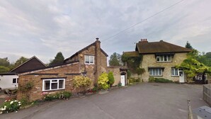 A two-story building with a brick facade, a front door, and a small garden with flowers. - Luxury 5BDR Riverside Retreat near Uxbridge (Harefield)