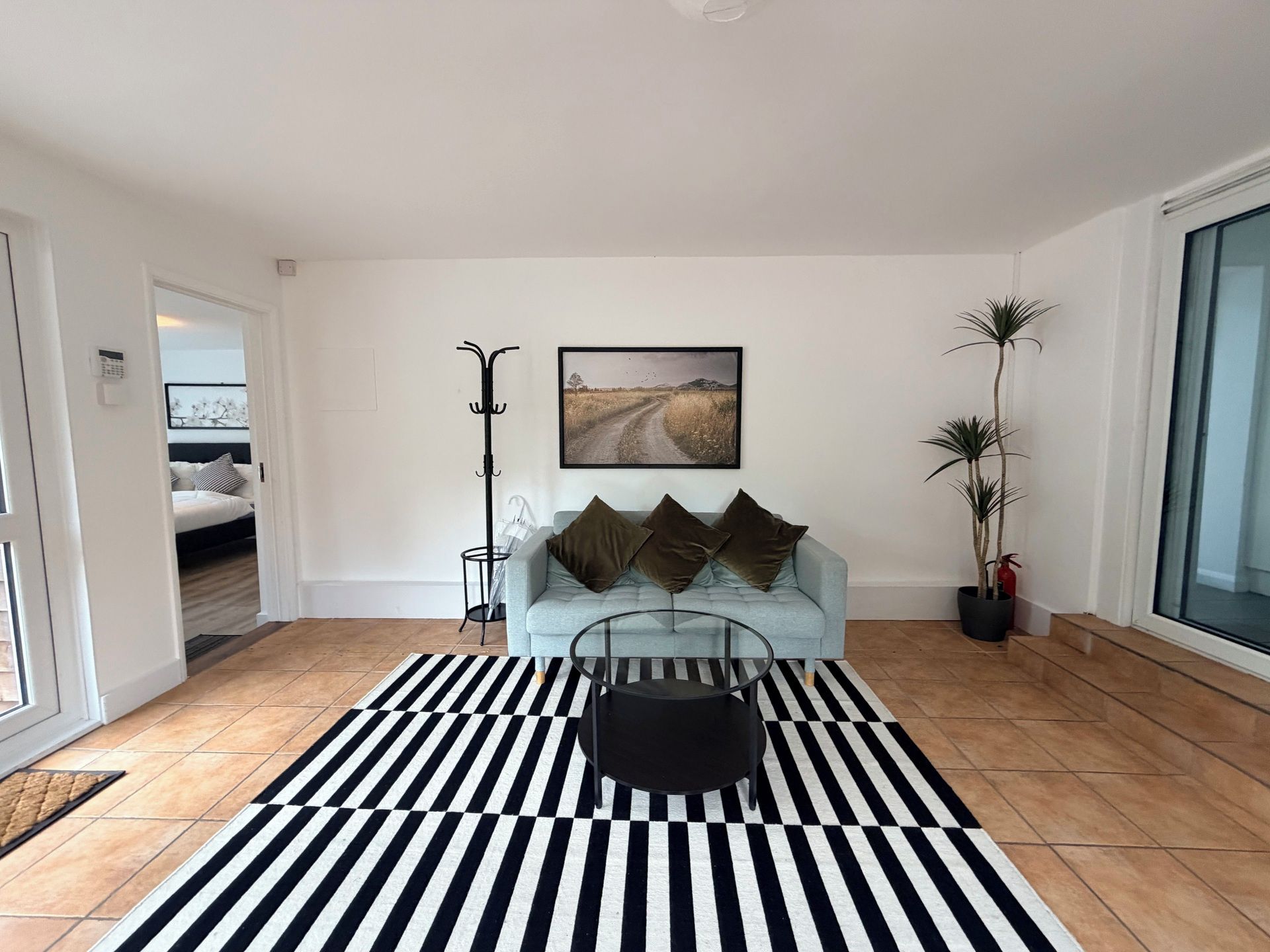Una sala de estar moderna con un sofá, una mesa de centro, un tapete a rayas blanco y negro, un cuadro enmarcado en la pared y una planta en maceta.