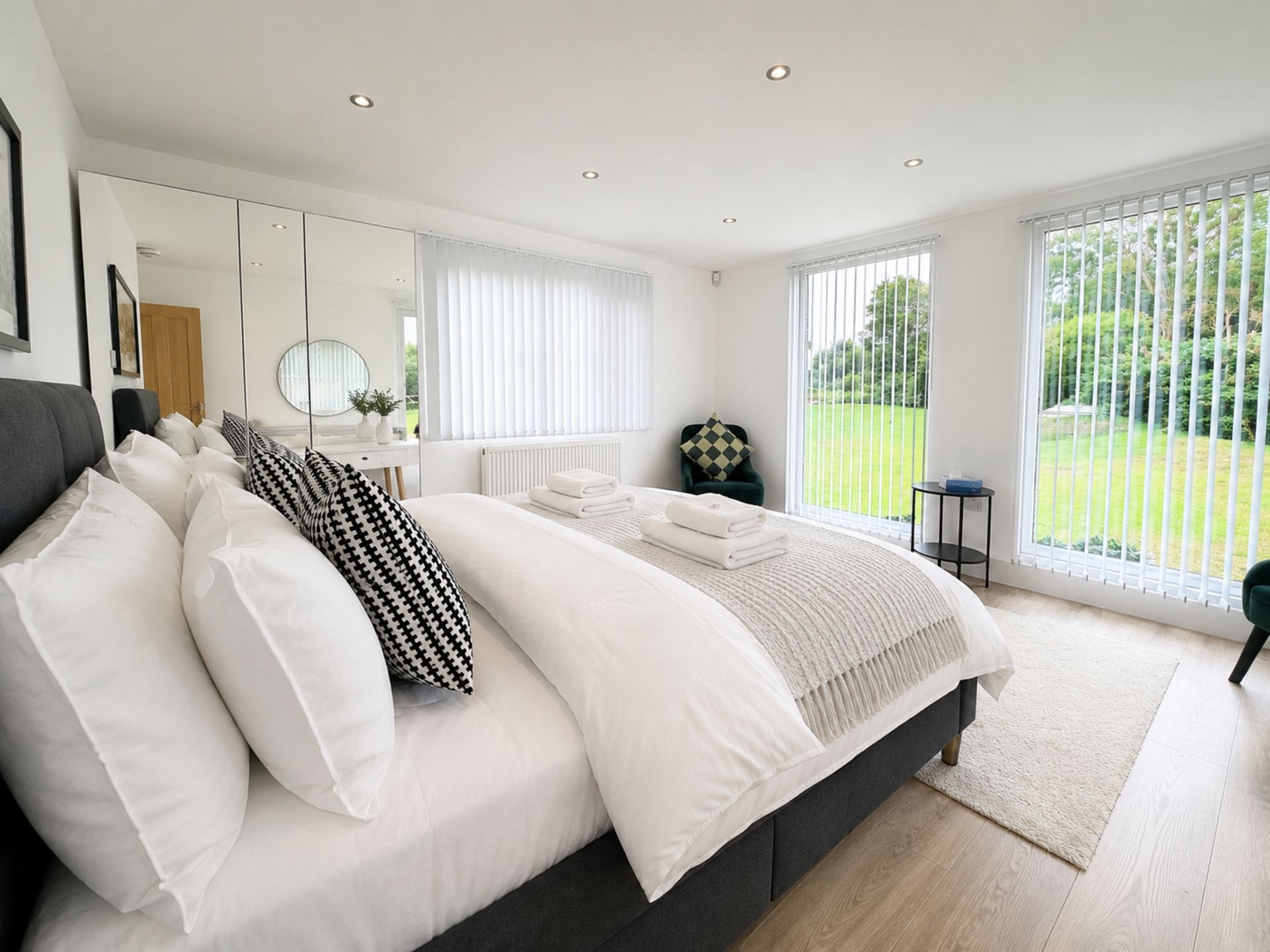 A modern bedroom with a large bed, a mirror, and a view of a garden through the window.