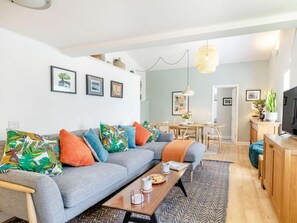 A modern living room with a grey sofa, colorful cushions, a wooden coffee table, and a dining area with a wooden table and chairs. - 2 Bed in Taunton (oc-88884) (Isle Brewers)