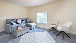 A living room with a grey sofa, a coffee table, a white armchair, and a patterned rug. - The Porterhouse - Residence II (Winchester)