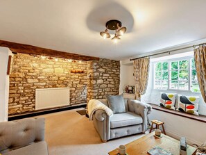 Ein gemütliches Wohnzimmer mit Steinwand, grauem Sofa, Couchtisch und einem fenster mit Vorhängen.