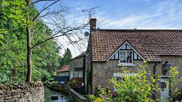 A stone building with a tiled roof, a narrow water channel, and lush greenery. - 2 Bed in Pickering (oc-88971) (Thornton Dale)