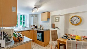 A kitchen with wooden cabinets, a built-in oven, a dining area with a table and chairs, and a wall clock. - 2 Bed in Pickering (oc-88971) (Thornton Dale)