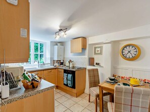 Eine Küche mit Holzschränken, einem eingebauten Backofen, einem Essbereich mit Tisch und Stühlen sowie einer Wanduhr.