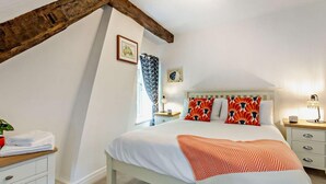 A bedroom with a sloped ceiling, a bed with patterned pillows, a nightstand with a lamp, and a window with curtains. - 2 Bed in Pickering (oc-88971) (Thornton Dale)