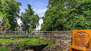 A garden with a stone wall, an anvil, and a wooden bench with an owl carving. - 2 Bed in Pickering (oc-88971) (Thornton Dale)