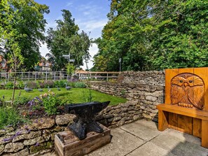 Ein Garten mit einer Steinmauer, einer Amboss und einer hölzernen Bank mit einer Eule geschnitzt.