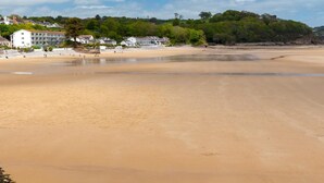 Ein Strand mit sandigem Ufer, Gebäuden im Hintergrund und wolkenlosem Himmel.