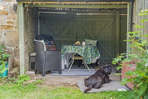 A rustic outdoor seating area with a table, chairs, and a dog. - 1 Bed in Hexham (oc-89085) (Bellingham)