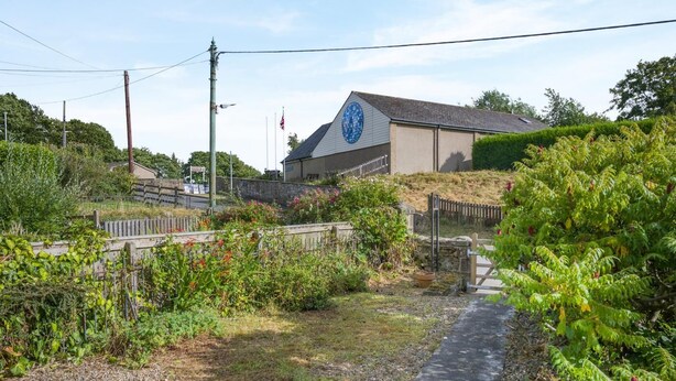 En bygning med et blåt rundt vindue, omgivet af grøn vegetation og en grussti.