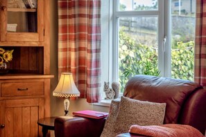 Une pièce chaleureuse avec un canapé en cuir, un meuble en bois, une table avec une lampe et une fenêtre avec des rideaux.
