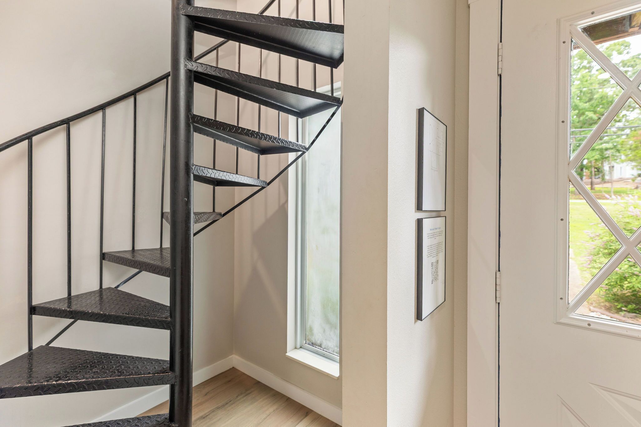A black spiral staircase in a room with a window and framed pictures on the wall.