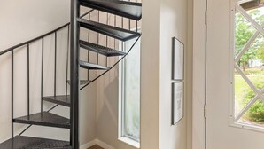 A black spiral staircase in a room with a window and framed pictures on the wall.