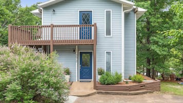 A two-story house with a front porch, a blue door, and a small front yard with plants.