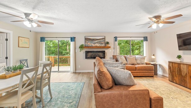A spacious living area with a sofa, dining table, ceiling fans, and a TV mounted on the wall.