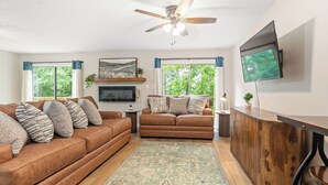A living room with a brown leather sofa, a wooden cabinet, a ceiling fan, and a flat-screen TV mounted on the wall.