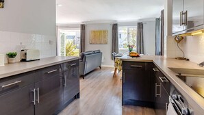 Uma cozinha moderna com armários escuros, uma ilha central e uma área de jantar com um sofá cinzento.
