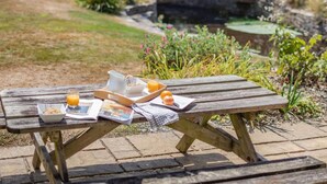 Uma mesa de piquenique de madeira com itens de café da manhã, uma revista e uma ponte ao fundo.