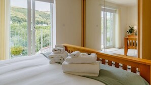 A hotel room with a bed, a large mirror, a bedside table with a lamp, and a view of a green landscape. - 4 Bed in Torpoint (oc-89135) (Deviock)