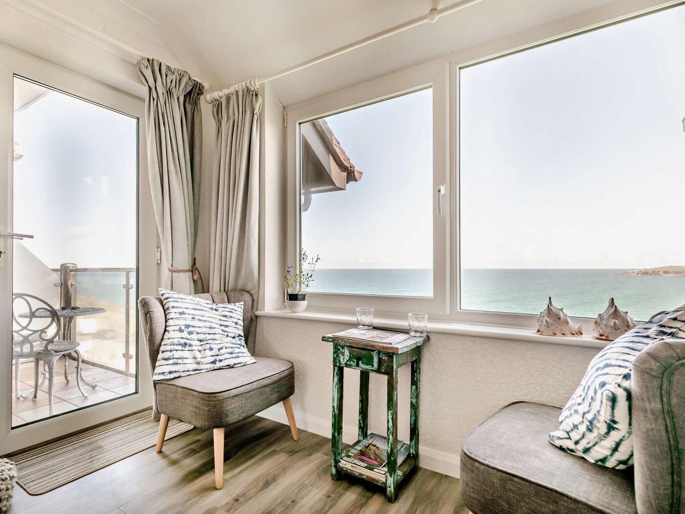 A cozy room with a view of the sea, a chair, a small table with books, and a window with curtains.