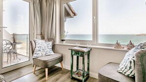 A cozy room with a view of the sea, a chair, a small table with books, and a window with curtains. - 1 Bed in Newquay (oc-89230) (Newquay)