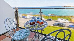 A balcony with a table set for tea, a chair, and a view of the sea and parked vehicles. - 1 Bed in Newquay (oc-89230) (Newquay)