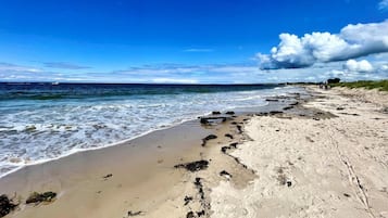 A beach with a clear sky, waves, and footprints in the sand.