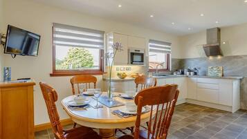 A dining area with a round table, wooden chairs, and a television mounted on the wall.