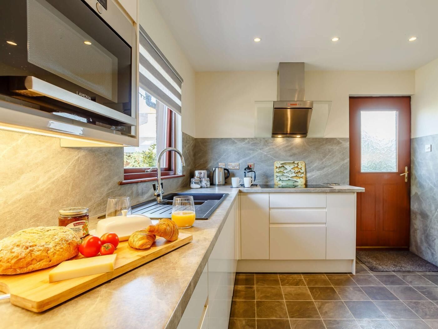 A modern kitchen with a built-in oven, stainless steel range hood, and a window.