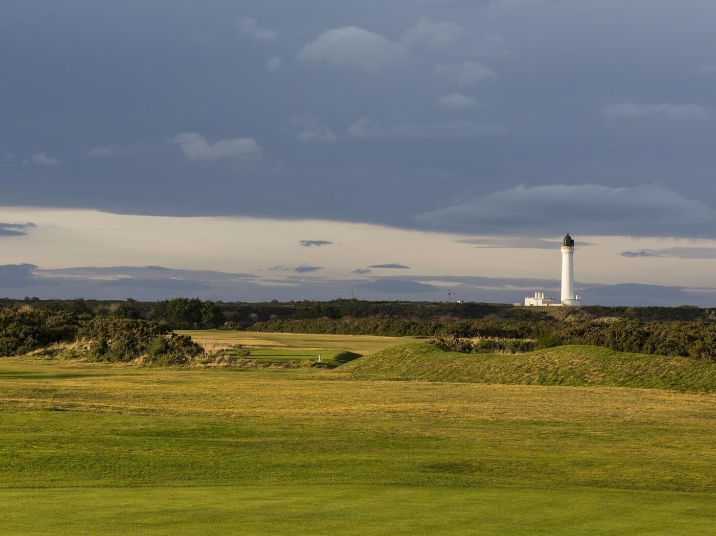 Un phare sur une colline herbeuse, sous un ciel nuageux.