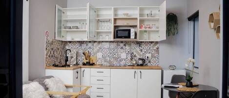 A compact kitchen with white cabinets, a microwave, and a tiled backsplash.