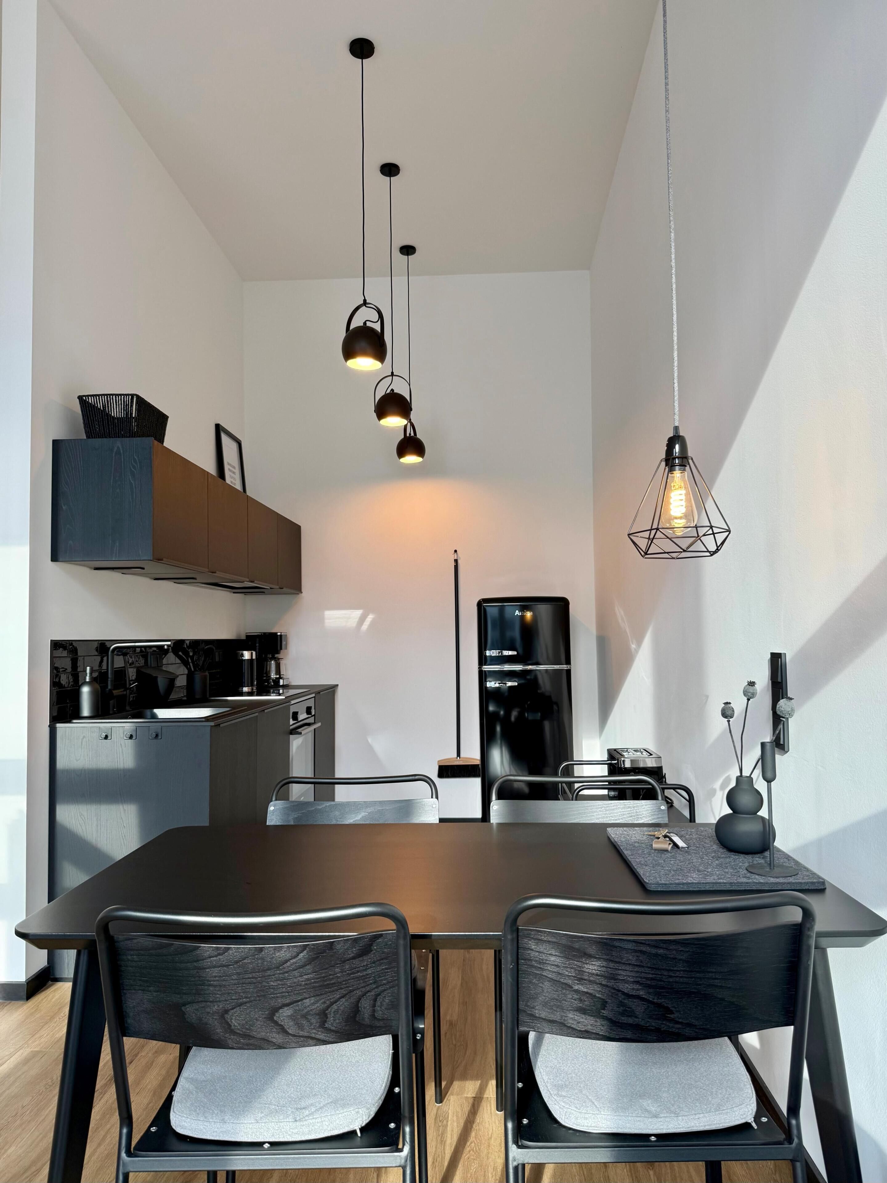 Una cocina moderna con comedor, que incluye una mesa, sillas y lámparas colgantes.