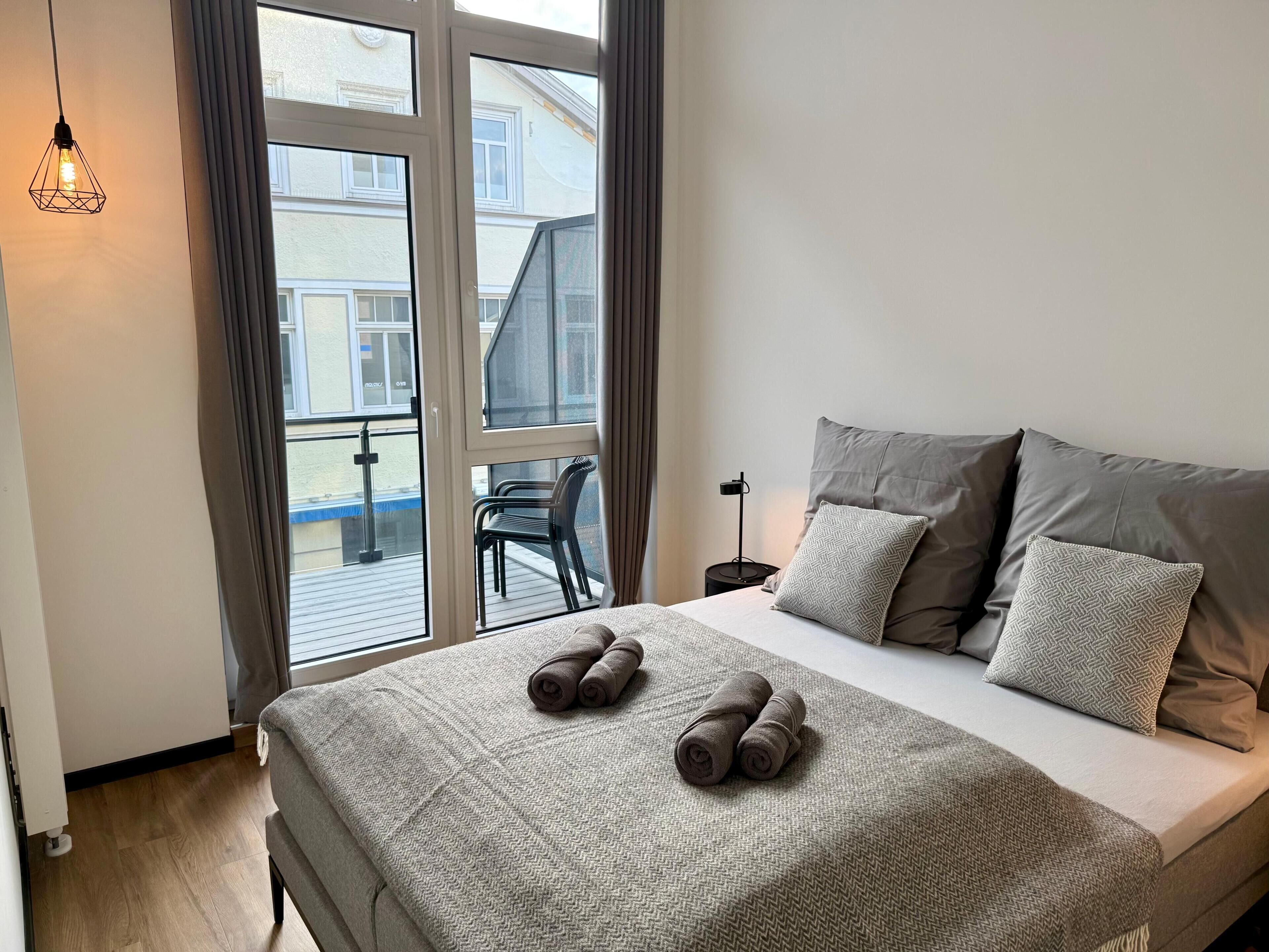 Een slaapkamer met een bed, kussens, een deken, een raam en uitzicht.