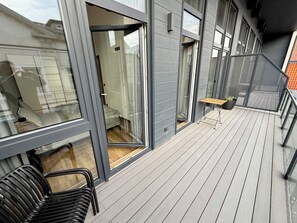 Een modern gebouw met grote ramen, een houten terras en een klein zitgedeelte.