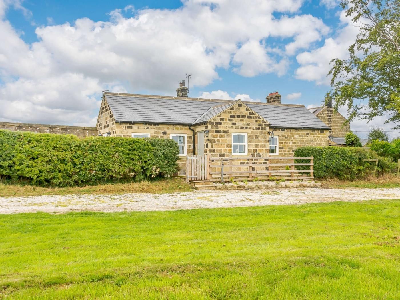 A stone house with a gravel driveway and a wooden fence.
