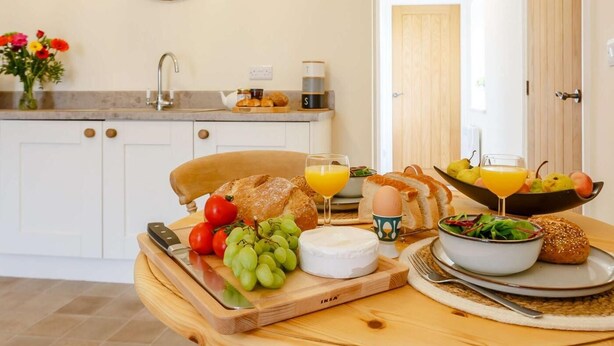 Ein Frühstück mit Brot, Käse, Tomaten, Trauben und einer Schüssel Salat auf einem Holztisch.