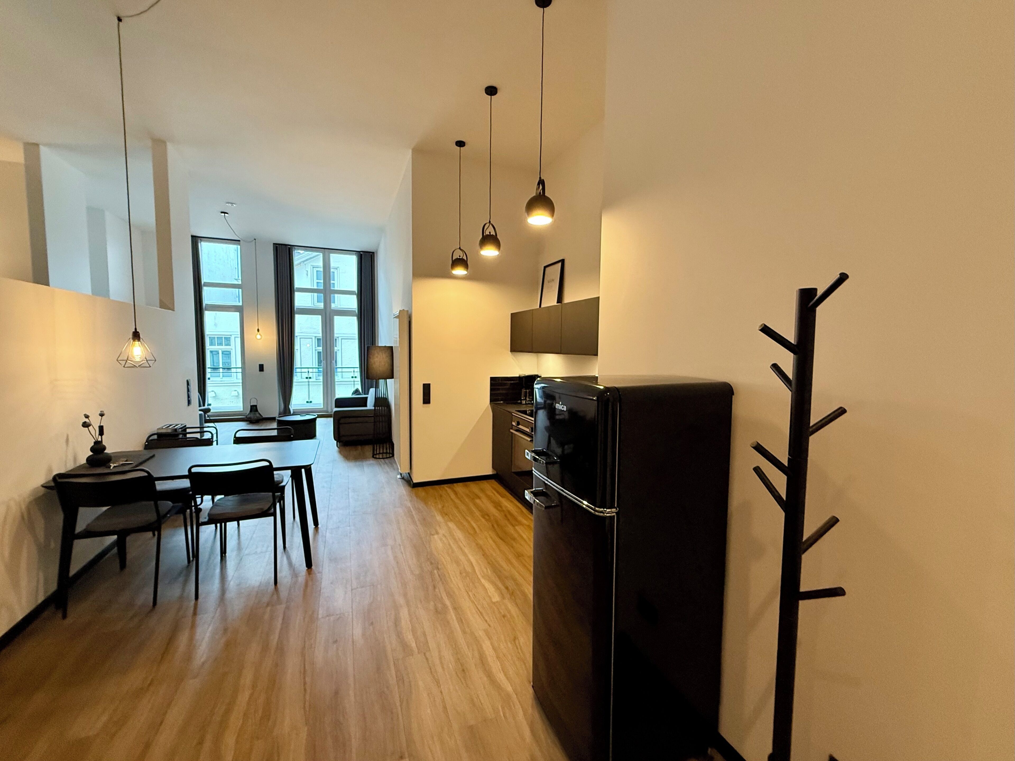 Eine moderne Küche mit einem schwarzen Kühlschrank, Holzböden und Pendelleuchten.
