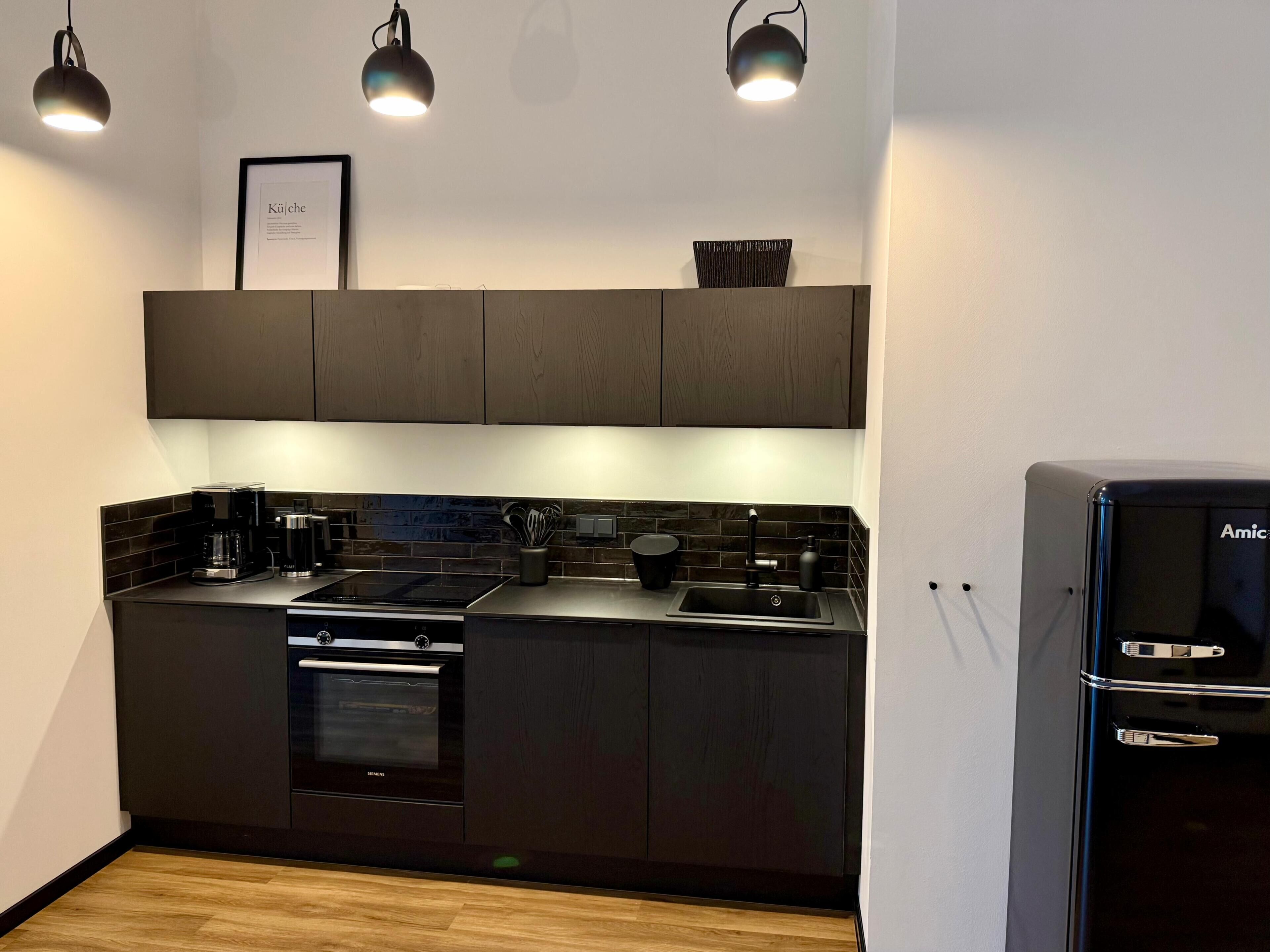 Eine moderne Küche mit dunklen Schränken, einem Backofen, einer Spüle und einem Kühlschrank.
