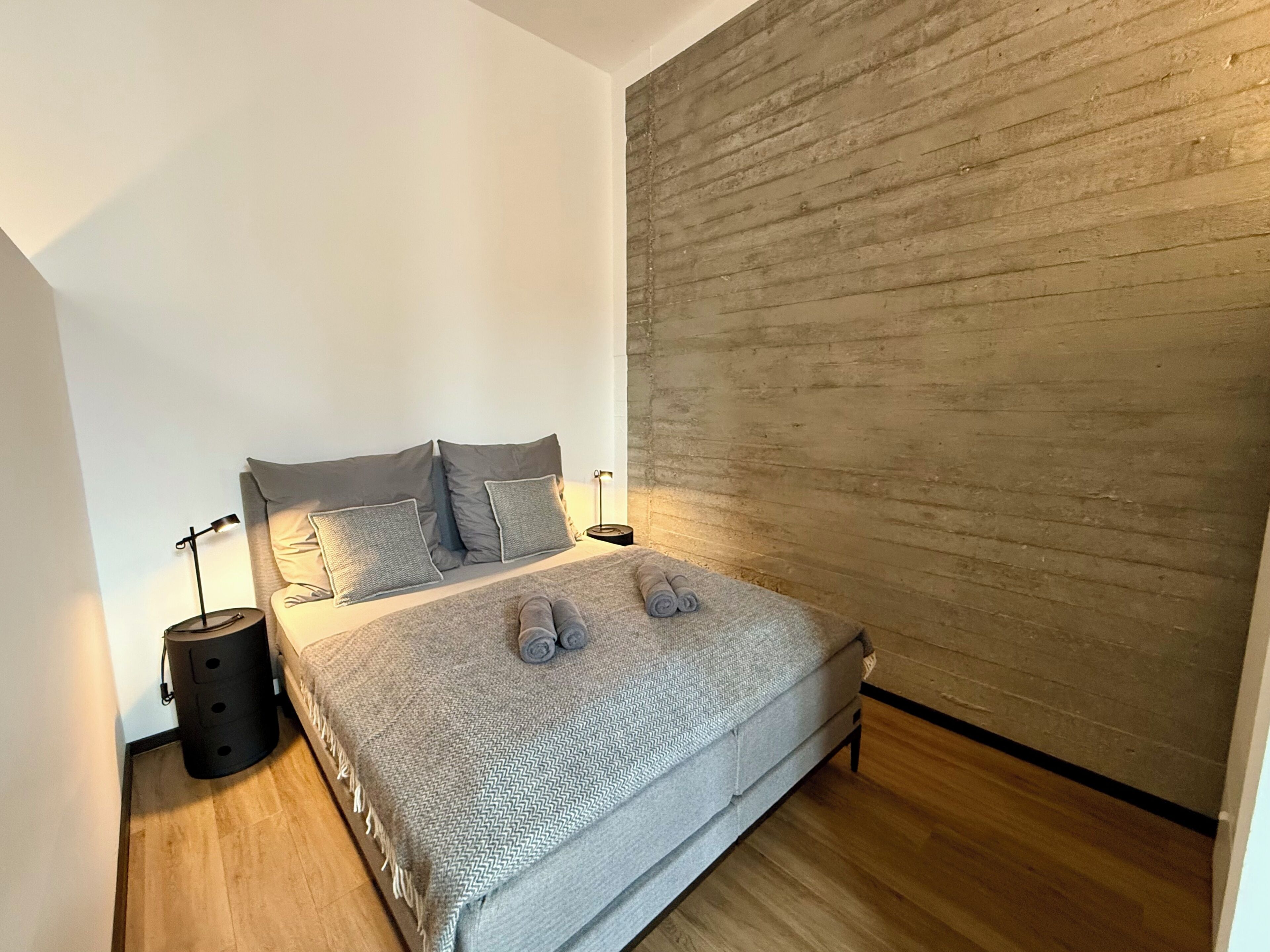 A bedroom with a bed, two bedside tables, a lamp, and a wooden wall.