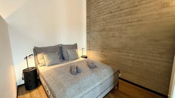 A bedroom with a bed, two bedside tables, a lamp, and a wooden wall.