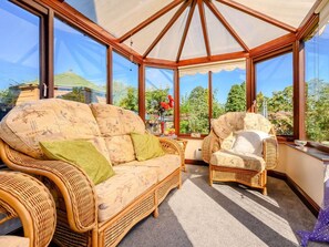 A conservatory with wicker furniture, large windows, and a view of greenery. - 3 Bed in Penrith (oc-89268) (Newton Reigny)